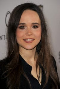 A smiling Ellen Page looks to the camera at a red carpet event wearing her hair long, straight, and down