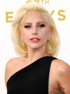 Lady Gaga smirks to the camera wearing a one-shoulder black dress