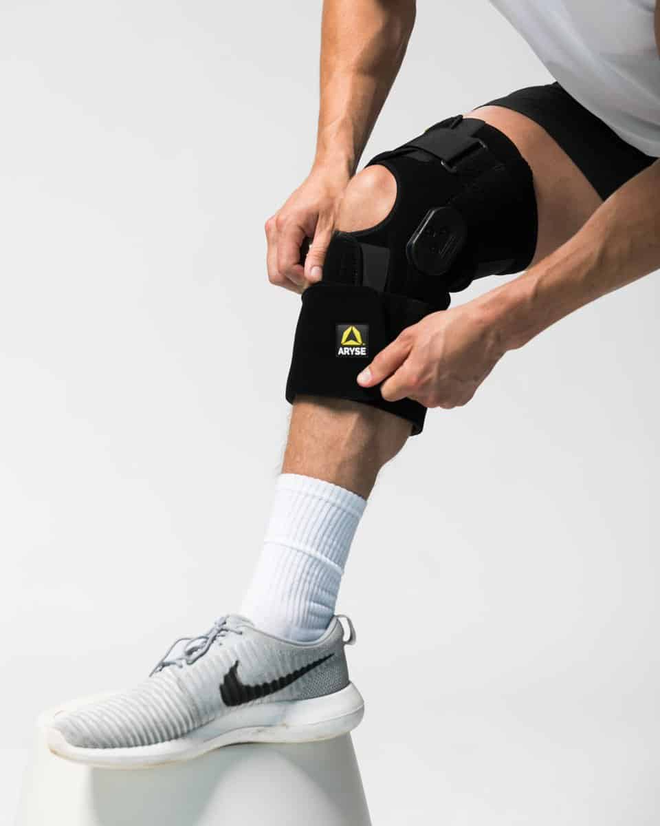 An athlete fastens the velcro straps of his knee brace with an open-patella design