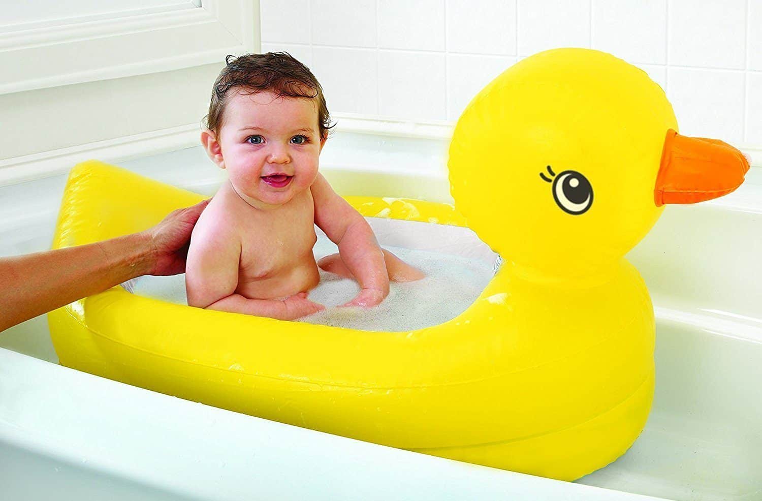 A small child looks at the camera and smiles while sitting inside their Munchkin White Hot Inflatable Duck Tub for babies